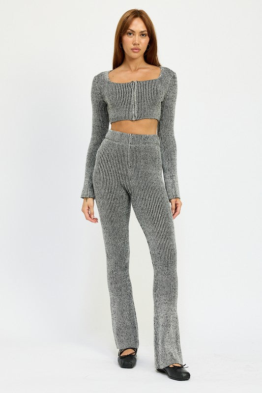 A person with long hair is wearing a grey, ribbed SQUARE NECK CROPPED TOP WITH ZIPPER, made from 60% cotton and paired with high-waisted pants. They are standing and looking directly at the camera. The model wears size small.