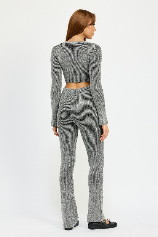 A person with long hair is wearing a grey, ribbed SQUARE NECK CROPPED TOP WITH ZIPPER, made from 60% cotton and paired with high-waisted pants. They are standing and looking directly at the camera. The model wears size small.