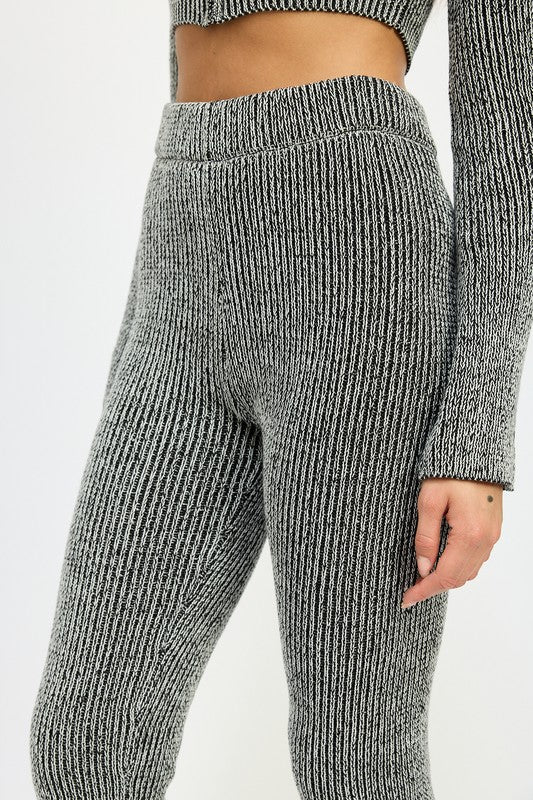 A person wearing HIGH WAIST RIBED PANTS and a grey knit long-sleeve crop top, made from 60% cotton, size small, standing against a plain background.