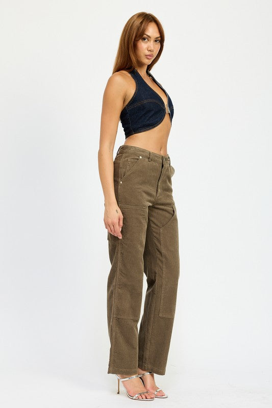 A person with long brown hair wearing the CROPPED HALTER DENIM TOP and brown corduroy pants made from 100% cotton stands against a plain background.