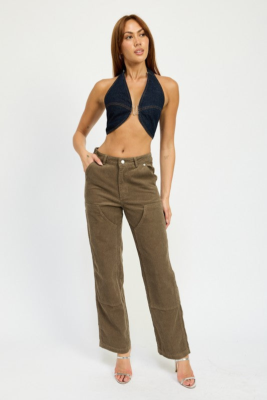 A person with long brown hair wearing the CROPPED HALTER DENIM TOP and brown corduroy pants made from 100% cotton stands against a plain background.