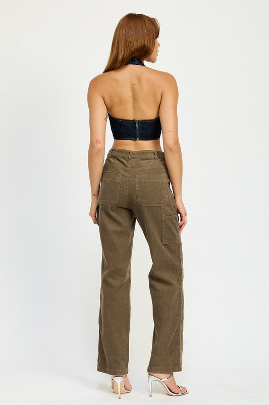 A person with long brown hair wearing the CROPPED HALTER DENIM TOP and brown corduroy pants made from 100% cotton stands against a plain background.