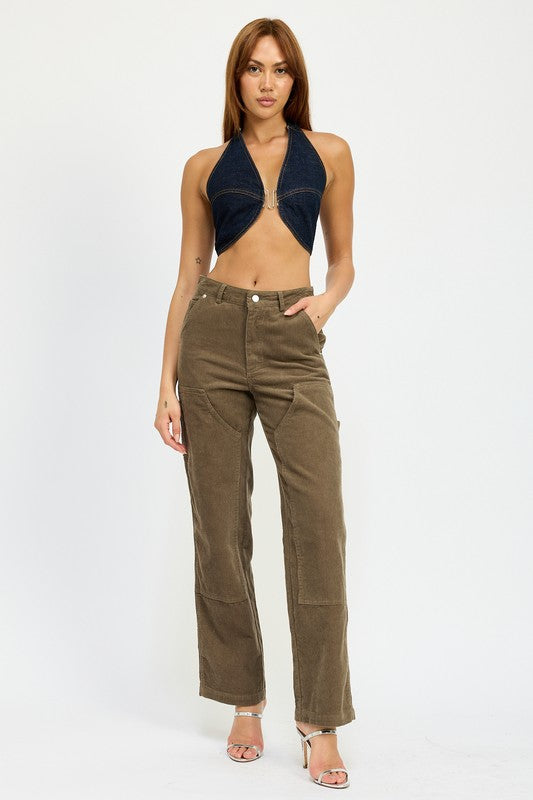 A person with long brown hair wearing the CROPPED HALTER DENIM TOP and brown corduroy pants made from 100% cotton stands against a plain background.