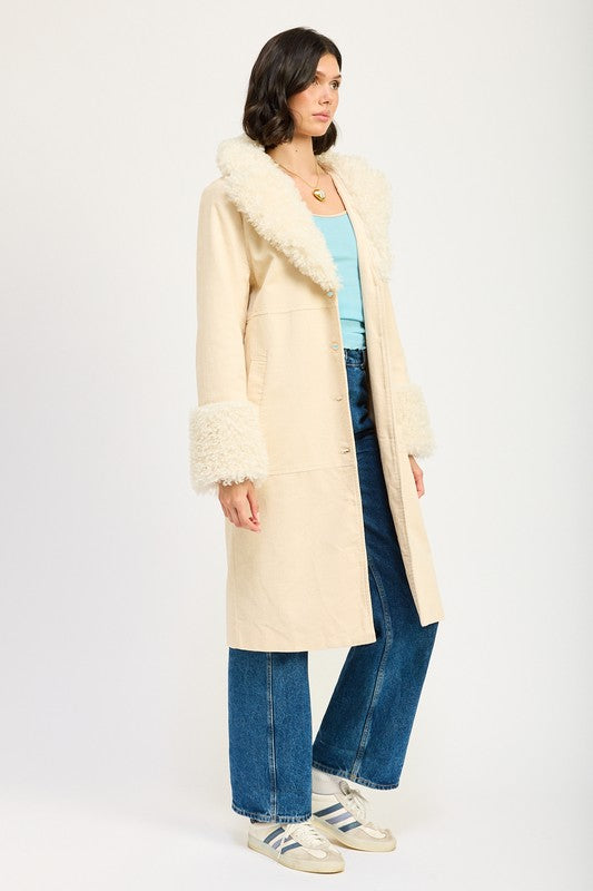 A woman in a blue top, jeans, and sneakers, wearing the FAUX FUR MID TRENCH COAT in beige with white fur trim on the collar and cuffs, size small, stands against a plain background.