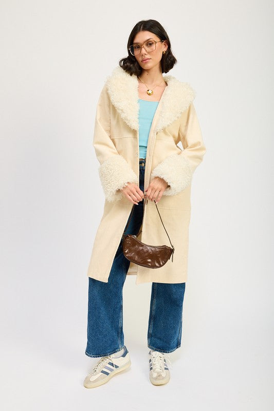 A woman in a blue top, jeans, and sneakers, wearing the FAUX FUR MID TRENCH COAT in beige with white fur trim on the collar and cuffs, size small, stands against a plain background.