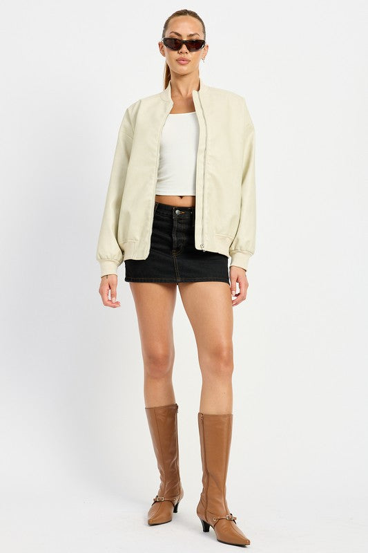 A person poses wearing a VINTAGE LEATHER BOMBER JACKET in maroon, made of polyurethane, over a white crop top and a black mini skirt, standing with hands in jacket pockets against a plain white background.