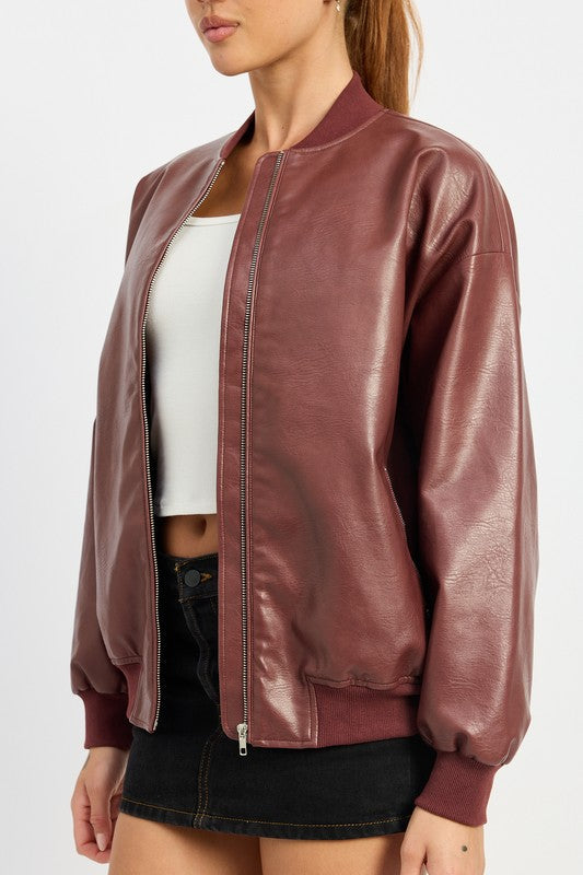 A person poses wearing a VINTAGE LEATHER BOMBER JACKET in maroon, made of polyurethane, over a white crop top and a black mini skirt, standing with hands in jacket pockets against a plain white background.