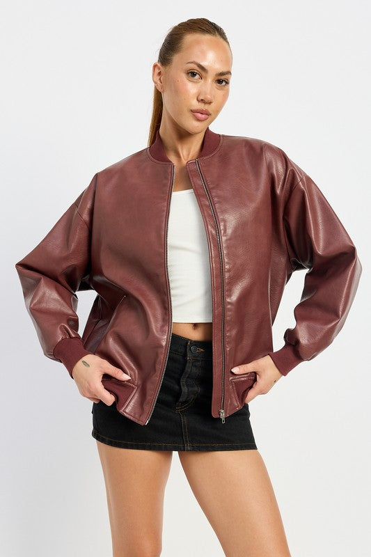 A person poses wearing a VINTAGE LEATHER BOMBER JACKET in maroon, made of polyurethane, over a white crop top and a black mini skirt, standing with hands in jacket pockets against a plain white background.