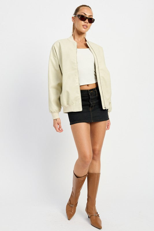 A person poses wearing a VINTAGE LEATHER BOMBER JACKET in maroon, made of polyurethane, over a white crop top and a black mini skirt, standing with hands in jacket pockets against a plain white background.