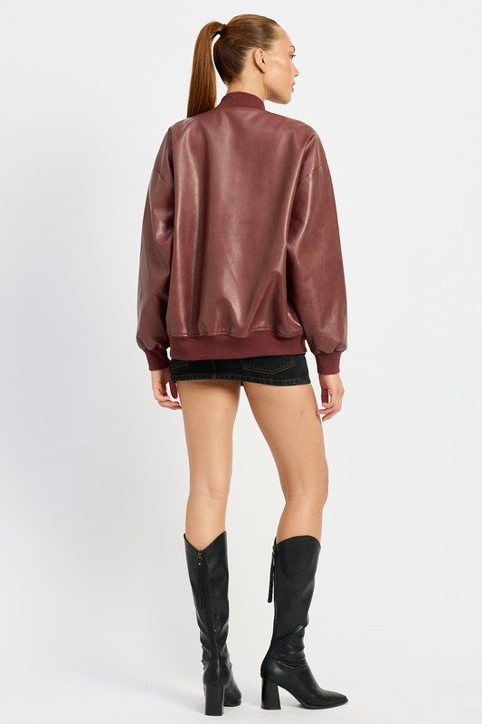 A person poses wearing a VINTAGE LEATHER BOMBER JACKET in maroon, made of polyurethane, over a white crop top and a black mini skirt, standing with hands in jacket pockets against a plain white background.