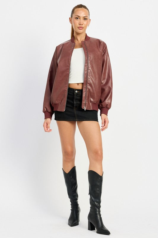 A person poses wearing a VINTAGE LEATHER BOMBER JACKET in maroon, made of polyurethane, over a white crop top and a black mini skirt, standing with hands in jacket pockets against a plain white background.