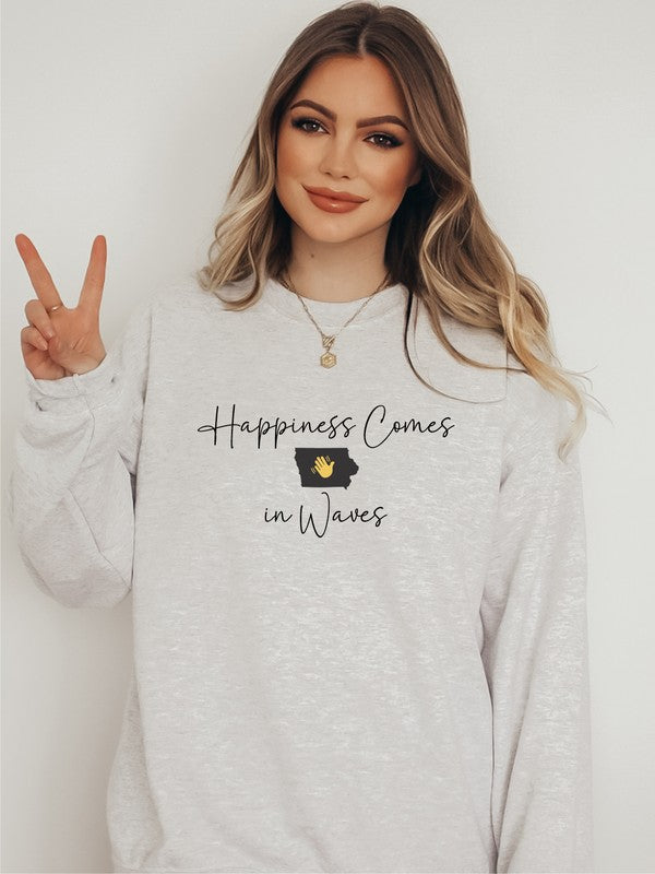 A person wearing the "Happiness Comes in Waves Cozy Sweatshirt," which features an illustration of a wave and a sun along with the text, effortlessly combines comfort and style. The unisex garment pairs perfectly with the person's long hair and orange-painted nails.