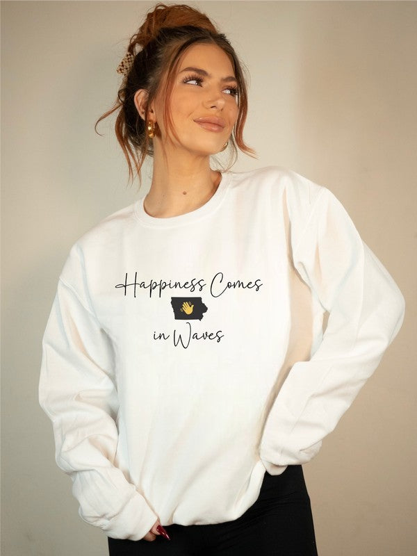 A woman with curly hair stands in front of a light blue background, holding a football while wearing the Happiness Comes in Waves Cozy Sweatshirt.