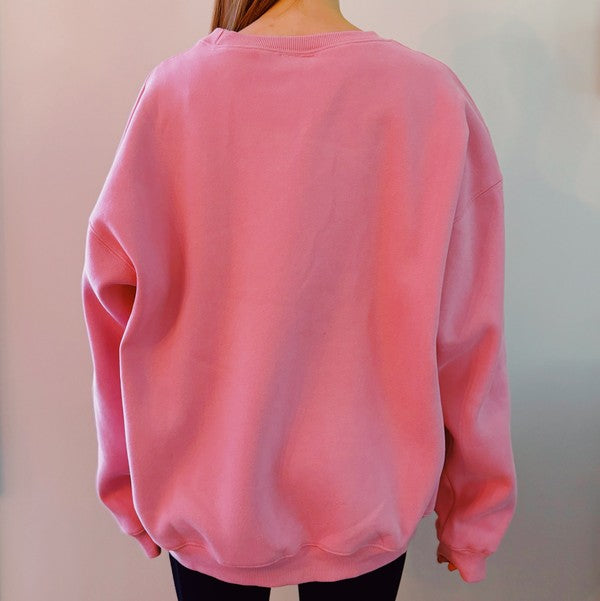 A person wearing a comfortable and stylish pink Paris Sweatshirt, a true wardrobe essential, sits on a white couch with arms resting on the backrest.