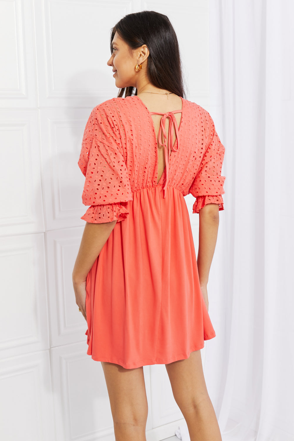 A person wearing the Ninexis Everyday Dreams Eyelet Contrast Dress, characterized by a romantic-style with an orange hue, featuring an eyelet-textured top and a flowing skirt, stands against a white background.