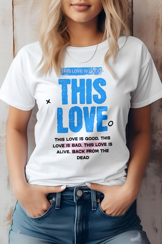 A person wearing the "This Love, Music Graphic Tee" by Bella Canvas, which features blue and black text inspired by Taylor Swift lyrics that reads "This Love is Good. This Love is Bad. This Love is Alive. Back from the Dead," stands with hands in their jeans pockets.