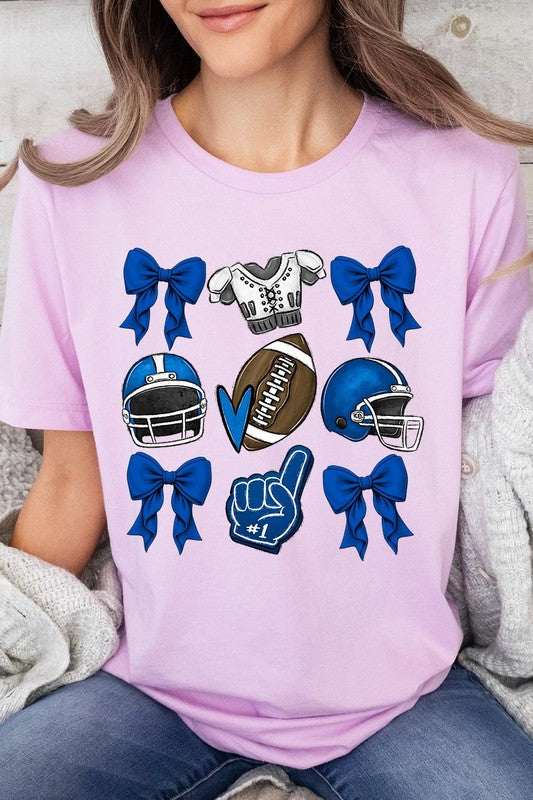 A woman wearing a Blue Coquette Football Graphic Tee adorned with blue bows, helmets, a football, a foam finger, and a jersey. She has yellow painted nails and is holding her shirt. This high-quality printed design guarantees long-lasting wear and vibrant colors.