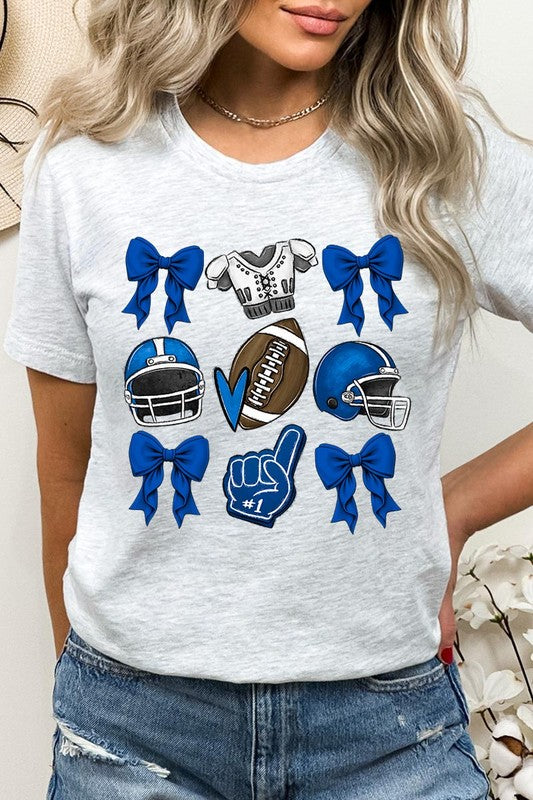 A woman wearing a Blue Coquette Football Graphic Tee adorned with blue bows, helmets, a football, a foam finger, and a jersey. She has yellow painted nails and is holding her shirt. This high-quality printed design guarantees long-lasting wear and vibrant colors.