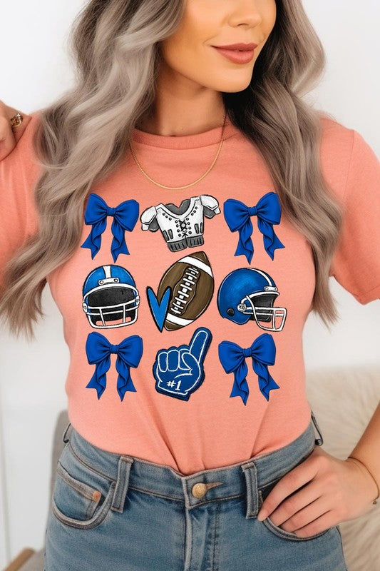 A woman wearing a Blue Coquette Football Graphic Tee adorned with blue bows, helmets, a football, a foam finger, and a jersey. She has yellow painted nails and is holding her shirt. This high-quality printed design guarantees long-lasting wear and vibrant colors.