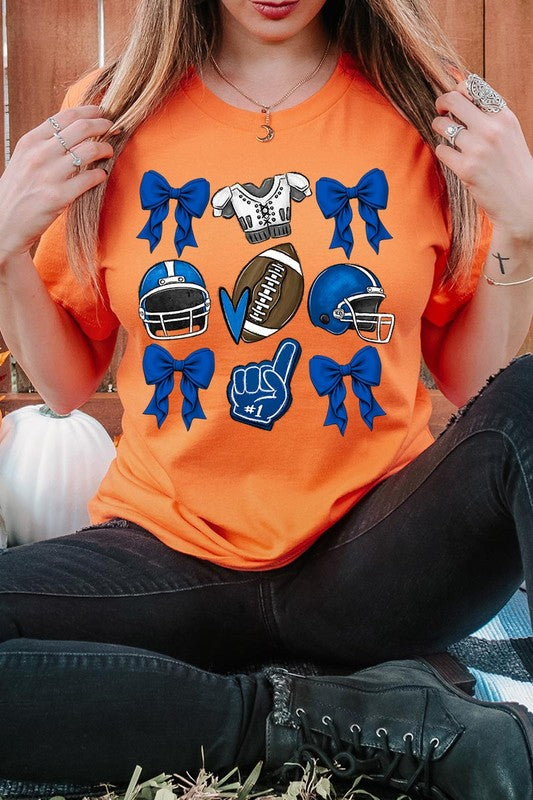 A woman wearing a Blue Coquette Football Graphic Tee adorned with blue bows, helmets, a football, a foam finger, and a jersey. She has yellow painted nails and is holding her shirt. This high-quality printed design guarantees long-lasting wear and vibrant colors.