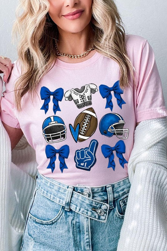 A woman wearing a Blue Coquette Football Graphic Tee adorned with blue bows, helmets, a football, a foam finger, and a jersey. She has yellow painted nails and is holding her shirt. This high-quality printed design guarantees long-lasting wear and vibrant colors.