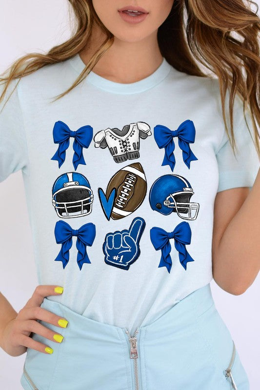 A woman wearing a Blue Coquette Football Graphic Tee adorned with blue bows, helmets, a football, a foam finger, and a jersey. She has yellow painted nails and is holding her shirt. This high-quality printed design guarantees long-lasting wear and vibrant colors.