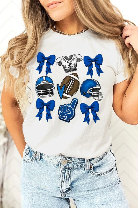 A woman wearing a Blue Coquette Football Graphic Tee adorned with blue bows, helmets, a football, a foam finger, and a jersey. She has yellow painted nails and is holding her shirt. This high-quality printed design guarantees long-lasting wear and vibrant colors.