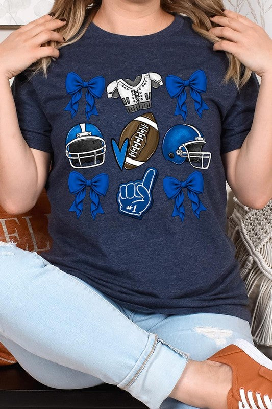 A woman wearing a Blue Coquette Football Graphic Tee adorned with blue bows, helmets, a football, a foam finger, and a jersey. She has yellow painted nails and is holding her shirt. This high-quality printed design guarantees long-lasting wear and vibrant colors.