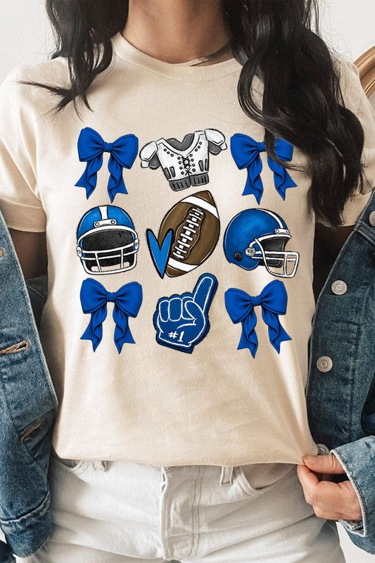 A woman wearing a Blue Coquette Football Graphic Tee adorned with blue bows, helmets, a football, a foam finger, and a jersey. She has yellow painted nails and is holding her shirt. This high-quality printed design guarantees long-lasting wear and vibrant colors.