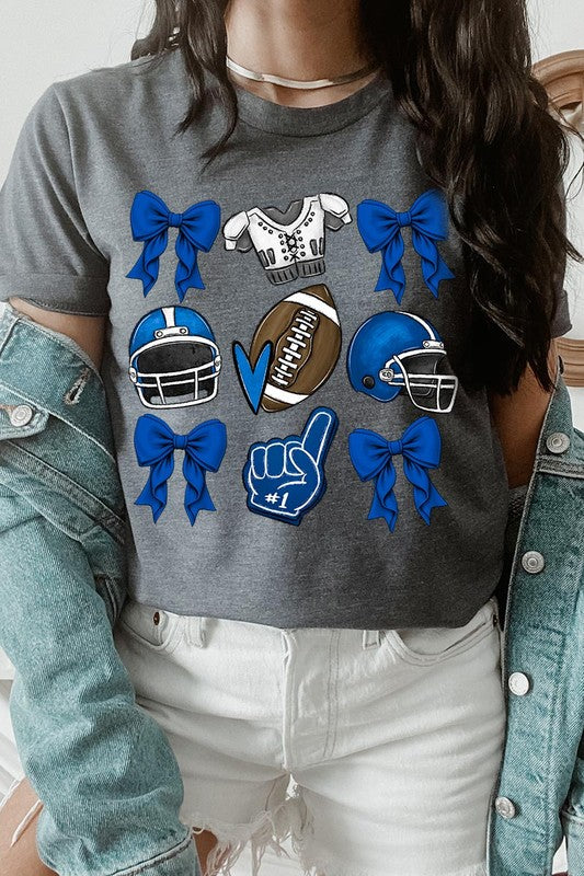 A woman wearing a Blue Coquette Football Graphic Tee adorned with blue bows, helmets, a football, a foam finger, and a jersey. She has yellow painted nails and is holding her shirt. This high-quality printed design guarantees long-lasting wear and vibrant colors.