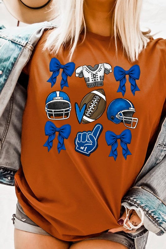 A woman wearing a Blue Coquette Football Graphic Tee adorned with blue bows, helmets, a football, a foam finger, and a jersey. She has yellow painted nails and is holding her shirt. This high-quality printed design guarantees long-lasting wear and vibrant colors.