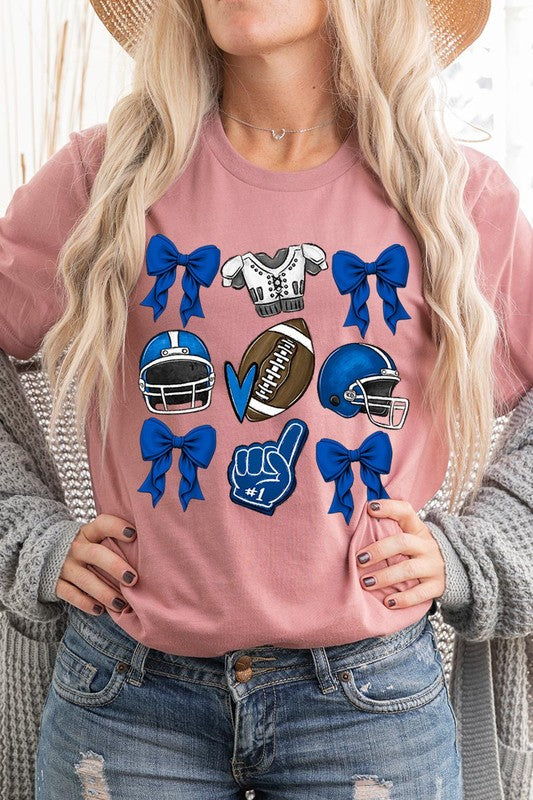 A woman wearing a Blue Coquette Football Graphic Tee adorned with blue bows, helmets, a football, a foam finger, and a jersey. She has yellow painted nails and is holding her shirt. This high-quality printed design guarantees long-lasting wear and vibrant colors.