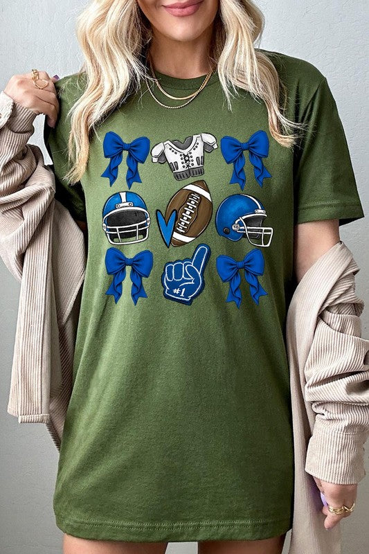 A woman wearing a Blue Coquette Football Graphic Tee adorned with blue bows, helmets, a football, a foam finger, and a jersey. She has yellow painted nails and is holding her shirt. This high-quality printed design guarantees long-lasting wear and vibrant colors.