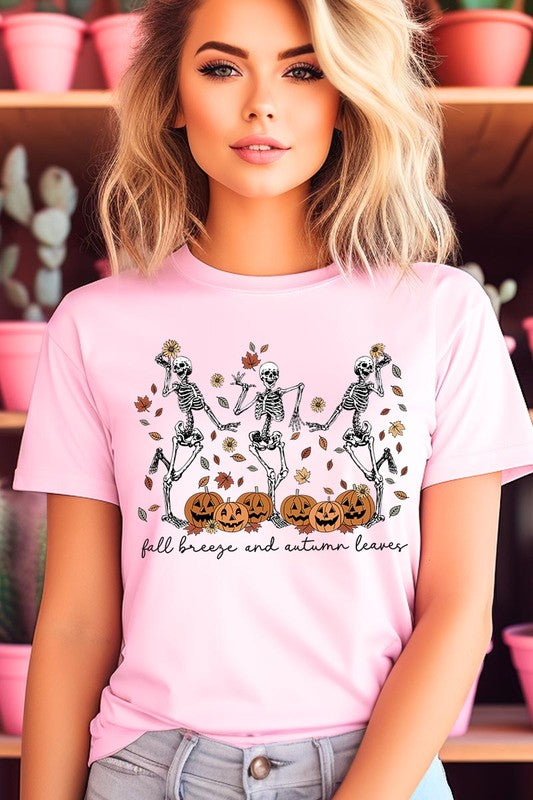 A person wearing a high-quality, unisex dark grey "Fall Breeze and Autumn Leaves Skeleton Graphic Tee" featuring dancing skeletons, pumpkins, and autumn leaves, holding an orange mug. They are dressed in a knitted cardigan and ripped jeans. The text on the shirt reads "Fall breeze and autumn leaves.