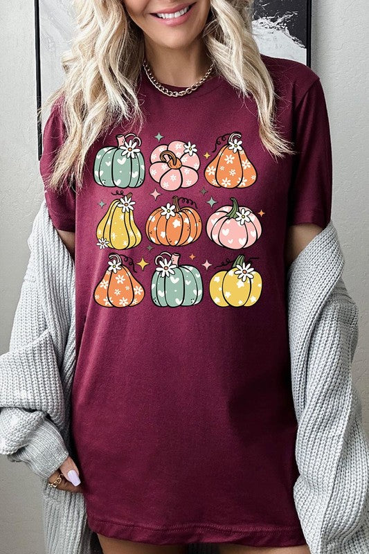 Person wearing a white Pumpkins & Daisies Retro Fall Graphic Tee featuring colorful, cartoonish pumpkins in various shapes and designs, beneath an open jean jacket.