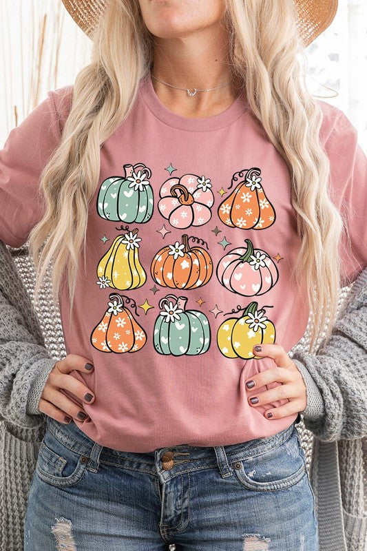 Person wearing a white Pumpkins & Daisies Retro Fall Graphic Tee featuring colorful, cartoonish pumpkins in various shapes and designs, beneath an open jean jacket.