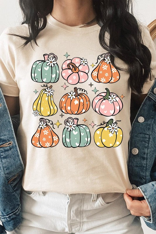 Person wearing a white Pumpkins & Daisies Retro Fall Graphic Tee featuring colorful, cartoonish pumpkins in various shapes and designs, beneath an open jean jacket.