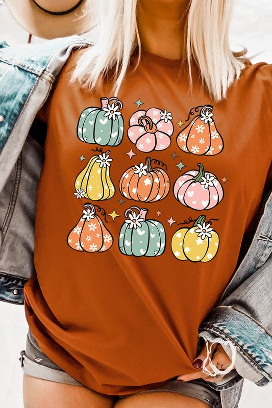 Person wearing a white Pumpkins & Daisies Retro Fall Graphic Tee featuring colorful, cartoonish pumpkins in various shapes and designs, beneath an open jean jacket.