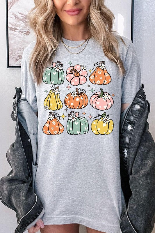 Person wearing a white Pumpkins & Daisies Retro Fall Graphic Tee featuring colorful, cartoonish pumpkins in various shapes and designs, beneath an open jean jacket.