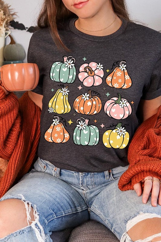 Person wearing a white Pumpkins & Daisies Retro Fall Graphic Tee featuring colorful, cartoonish pumpkins in various shapes and designs, beneath an open jean jacket.