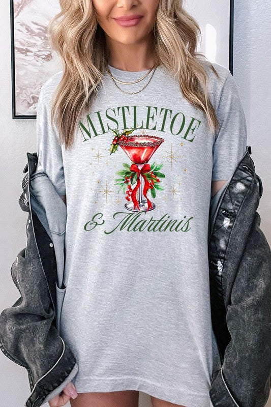 A person wearing the high-quality "Mistletoe & Martinis Graphic Tee" that features festive text and graphics, including a martini glass illustration adorned with holiday decorations, paired with a green plaid shirt.