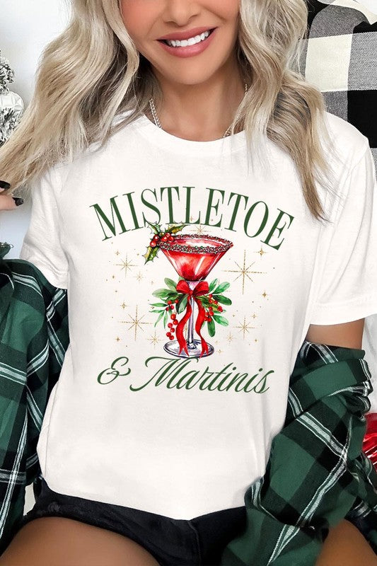 A person wearing the high-quality "Mistletoe & Martinis Graphic Tee" that features festive text and graphics, including a martini glass illustration adorned with holiday decorations, paired with a green plaid shirt.