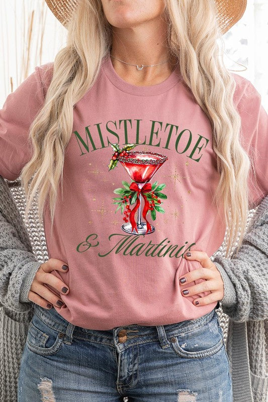 A person wearing the high-quality "Mistletoe & Martinis Graphic Tee" that features festive text and graphics, including a martini glass illustration adorned with holiday decorations, paired with a green plaid shirt.