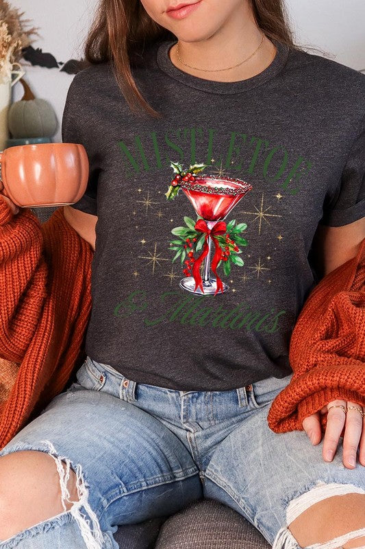 A person wearing the high-quality "Mistletoe & Martinis Graphic Tee" that features festive text and graphics, including a martini glass illustration adorned with holiday decorations, paired with a green plaid shirt.