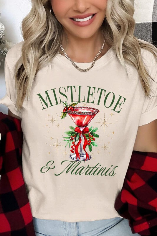 A person wearing the high-quality "Mistletoe & Martinis Graphic Tee" that features festive text and graphics, including a martini glass illustration adorned with holiday decorations, paired with a green plaid shirt.