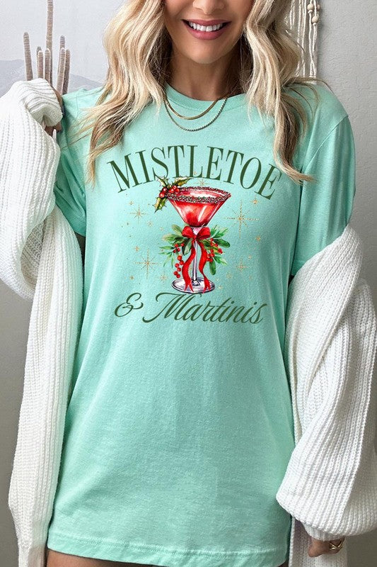 A person wearing the high-quality "Mistletoe & Martinis Graphic Tee" that features festive text and graphics, including a martini glass illustration adorned with holiday decorations, paired with a green plaid shirt.