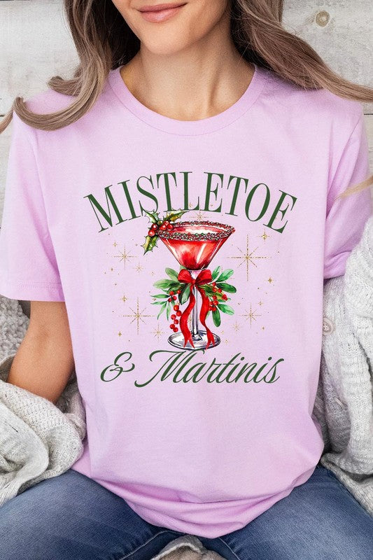 A person wearing the high-quality "Mistletoe & Martinis Graphic Tee" that features festive text and graphics, including a martini glass illustration adorned with holiday decorations, paired with a green plaid shirt.