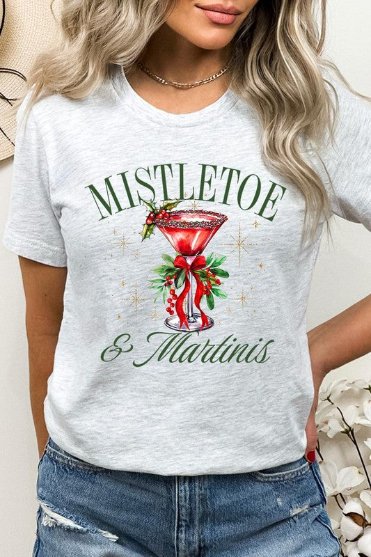 A person wearing the high-quality "Mistletoe & Martinis Graphic Tee" that features festive text and graphics, including a martini glass illustration adorned with holiday decorations, paired with a green plaid shirt.