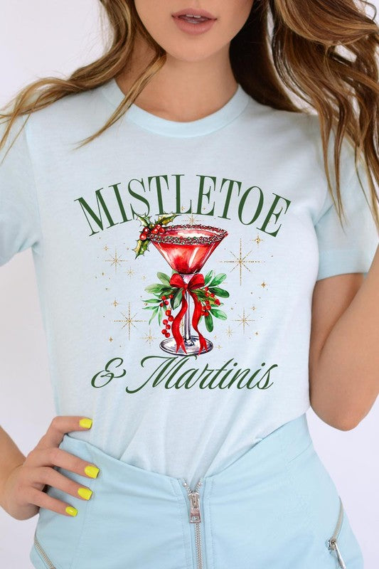 A person wearing the high-quality "Mistletoe & Martinis Graphic Tee" that features festive text and graphics, including a martini glass illustration adorned with holiday decorations, paired with a green plaid shirt.