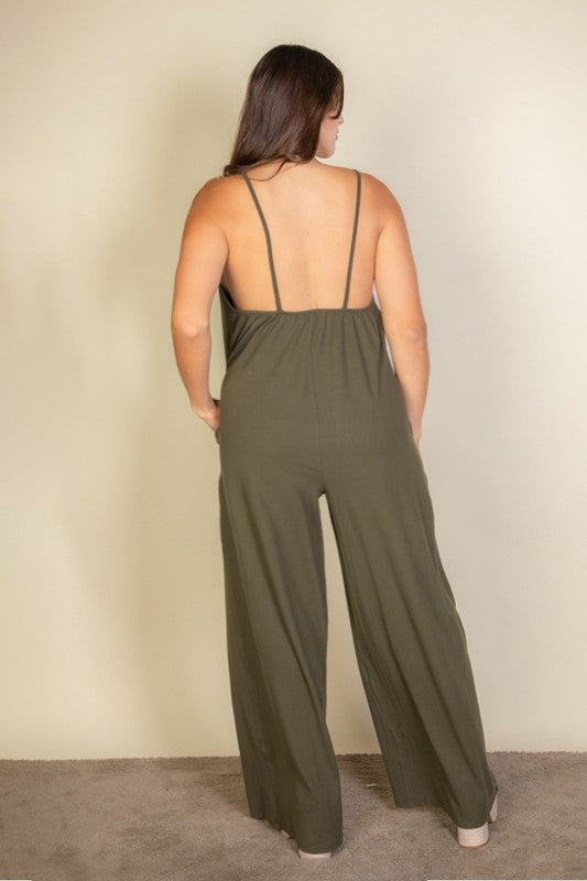 A woman in a Plus Spaghetti Strap Solid Wide Jumpsuit poses against a plain beige background. She has her hands in the pockets and is wearing platform sandals.